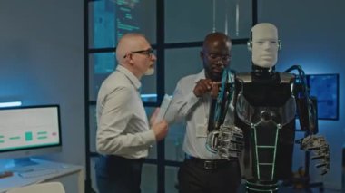 Laboratuvarda çalışan, robot gibi insanları tamir eden ve geliştiren çeşitli erkek robotik mühendislerinin orta boy görüntüleri.