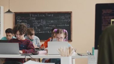 Çok ırklı bir grup gencin parlak modern sınıflarda masalarında oturup birlikte kodlama ve programlama okuması.