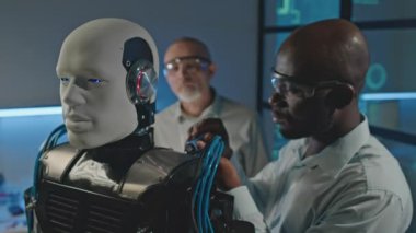 Bilim kurgu atölyesinde iş arkadaşıyla çalışırken insan gibi tornavidayla robot tamir eden konsantre siyah erkek robotik mühendisi.