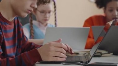 Okulda IT dersi sırasında dizüstü bilgisayarda klavye kullanan konsantre genç programcının orta ölçekli yakın çekimi