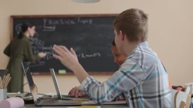 Beyaz tenli liseli bir çocuğun, programlama ve kodlama okurken kadın öğretmenlere soru sorması.