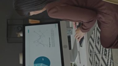 Bilgisayarda iş diyagramını analiz ederken, modern ofiste masa başında çalışırken, klavyede daktilo kullanan genç bir kadının dikey arka plan görüntüsü.