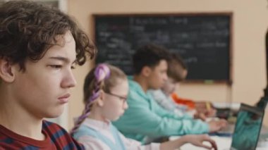 Modern sınıftaki programlama dersleri sırasında dizüstü bilgisayar kullanan konsantre ergen çift ırklı öğrencilerin orta boy yakın çekimi.