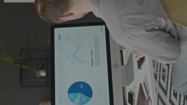 Modern ofiste çalışırken bilgisayar monitöründen iş diyagramına bakan beyaz erkek finansal analistin dikey görünümü