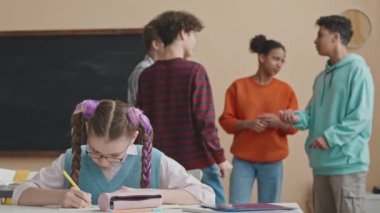 Sınıftaki çok ırklı sınıf arkadaşları arka planda sohbet ederken, siyah at kuyruklu beyaz liseli kızın göğsü açılır.