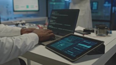 Koyu bilimsel ve araştırma laboratuvarında robot yazılım geliştirme üzerinde çalışırken, beyaz laboratuvar önlüklü, tanımlanamayan teknoloji geliştiricisinin laptopta program kodunu yazarken görüntüsü kesildi.