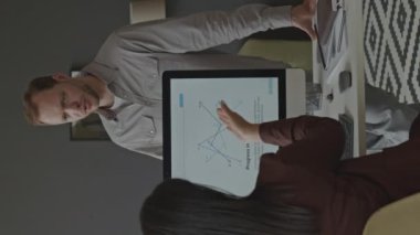 İş kadınının bilgisayar monitöründeki şirket mali ilerlemesinin grafiğiyle çalışma masasında oturup, erkek ofis çalışanı ile göstergeleri tartışırken dikey orta pozu