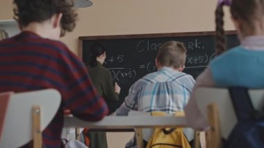 Modern sınıfta matematik dersi alırken öğrencinin sınıf arkadaşına kopya kağıdı uzatması.