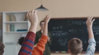 Çok ırklı ergen öğrenciler ders sırasında matematik denklemini çözmek için ellerini kaldırıyorlar.