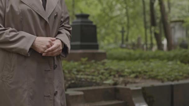 身着长战壕外套的无法辨认的女人的中间部分 她们手挽手站在墓地她心爱的人的坟墓旁 — 图库视频影像