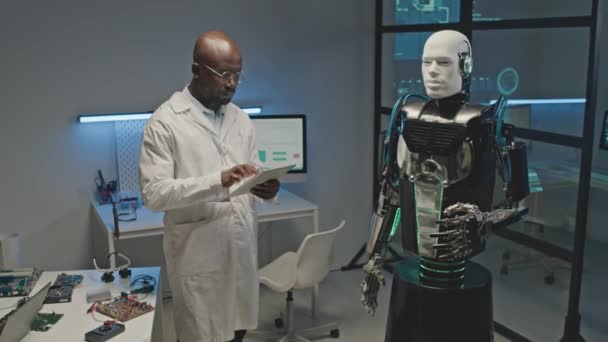 워크샵에서 로봇을 운영하는 디지털 태블릿을 사용하여 실험실 코트에 아프리카계 엔지니어의 — 비디오