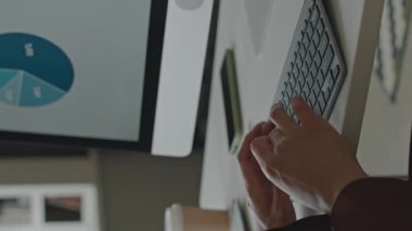 Ofisteki beyaz çalışma masasındaki bilgisayar ekranında finansal verileri analiz ederken klavyede tanımlanamayan kadınların ellerinin dikey görüntüsü.