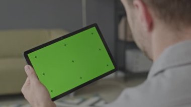 Gündüzleri modern ofiste çalışırken yeşil ekranlı dijital tablet kullanan bir adamın omzunun üstünden.