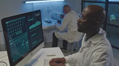 Yoğunlaştırılmış siyah erkek elektronik mühendisi karanlık laboratuarlarda mikroçipin veri bilgilerini inceleyecek.