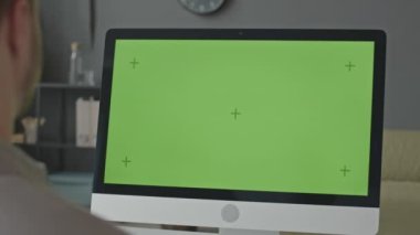 Erkek ofis çalışanının yeşil renkli anahtar şablonu olan bilgisayar ekranının önünde otururken çekilmiş omuz çekimi.
