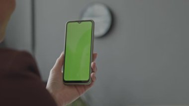 Krom anahtar yeşil ekranlı akıllı telefonu tutan tanımlanamayan bir kadının omzunun üstünden.