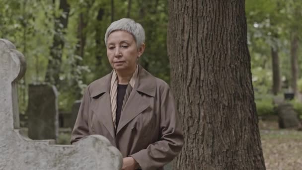 在墓地的墓碑前 一位亚洲老年妇女站在十字架墓碑旁 中等程度地哀悼 — 图库视频影像