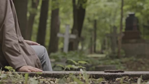 墓地だけで墓石の上に座っている認識できない女性のクロップショット — ストック動画