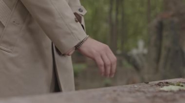 Mezarda elini soğuk granit mezar taşına koyan, deve hendeği paltolu tanınmayan bir adamın kırpılmış görüntüsü.