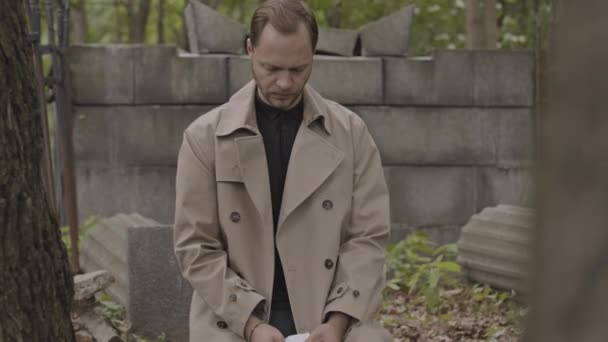 中镜头 年轻的白人男子坐在墓地冰冷的水泥石上哀伤 — 图库视频影像