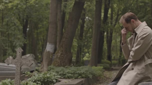 Скорбящий Кавказский Мужчина Плачет Сидя Гранитном Надгробии Среди Зеленых Деревьев — стоковое видео