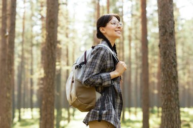 Sırt çantalı genç kız yazın ormanda yürüyüş yapıyor.