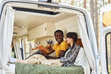 Tekerlekli evde dinlenen çok ırklı genç bir çift, yatakta oturup kitap okuyorlar.