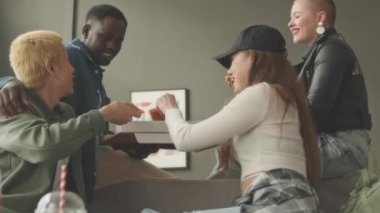 Dört çoklu etnik kökenli arkadaşın sohbet edip pizza yerken, hafta sonu apartmanda toplanırken eğlenirken orta boy bir fotoğraf.