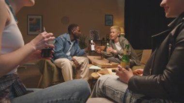 Çok ırklı erkek ve kız çocuklarının içki içip yemek yediği orta boy bir fotoğraf. Akşam birlikte apartman dairesinde vakit geçirirken bir yandan da fast food yiyor.