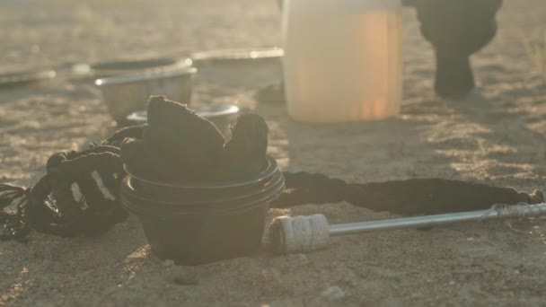 缶から金属製のボウルに灯油を注ぐ 日没の砂浜での火のショーの準備をしている認識できない人のゆっくりとした動き — ストック動画
