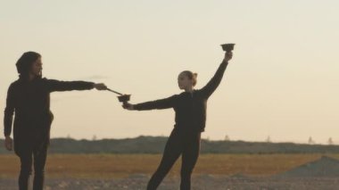 Gün batımında ateş gösterisi yapan iki profesyonel sirk sanatçısının yavaşlığı.