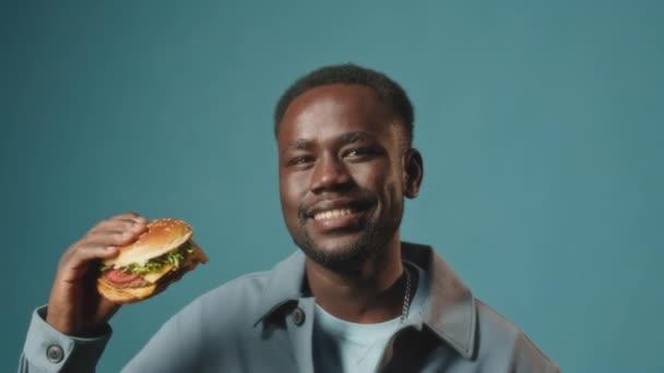 Portretul Tânărului Negru Zâmbind Aparatul Foto Ținând Burger Mare Delicios — Videoclip de stoc