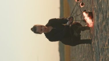 Kafkasyalı genç bir kadının günbatımında sanatsal ekstrem ateş gösterisi sırasında yangın yelpazesini yaktığı dikey çekim.