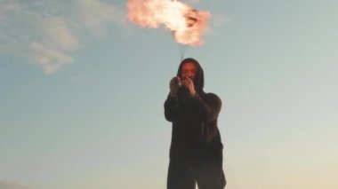 Genç profesyonel erkek sanatçının gün batımında ateş gösterisi yaparken iki yanan kadrosuyla hokkabazlık yaptığı orta boy bir fotoğraf.