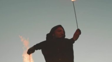 Günbatımında yangın gösterisi yaparken yanan zincirler kullanan genç profesyonel sirk sanatçısının orta boy fotoğrafı.