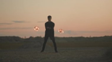 Yaz festivali sırasında gün batımında plajda itfaiye ekipmanlarıyla hokkabazlık yapan genç cesur beyaz adamın tam boy çekimi.