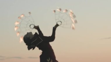 Otantik kostümlü cesur bir kızın gün batımında hayranlarıyla ateş gösterisi yaptığı orta boy bir fotoğraf.