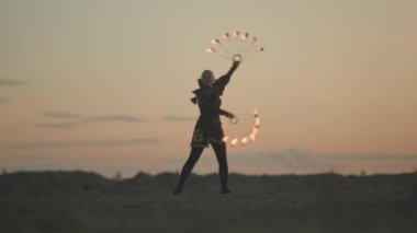 Kostümlü genç kadın sirk sanatçısının, altın sarısı günbatımında ateşle dans edişinin tam boy çekimi.