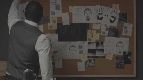 アフリカ系アメリカ人探偵の中央ビュー 証拠コルクボードに立って刑事事件情報が同一の容疑者と手形 新聞や犯罪現場の写真からの切断 — ストック動画