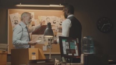 İki profesyonel çok ırklı FBI ajanının kanıt panosunda dikilip karanlık ofiste dava soruşturması üzerinde tartışırken orta boy bir fotoğrafı.