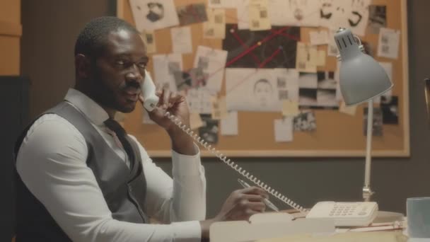 직업적인 아프리카계 미국인 형사의 사무실에서 책상에 앉아서 사례를 전화에 말하기 — 비디오