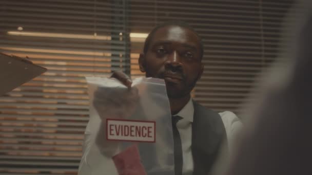 어두운 경찰서에서 심문하는 사람에게 봉투에 물리적 증거를 보여주는 아프리카계 Fbi — 비디오