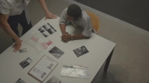 逮捕されたブラックマンは 尋問室の警察署にインタビューされている間に 犯罪現場からビニール袋と黒と白の写真の物理的証拠を見ている — ストック動画