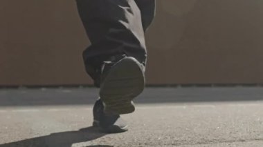 Güneşli bir sabahta açık havada antrenman yaparken, bol pantolonlu ve spor ayakkabılı, tanınmayan birinin alt kısmı ayaklarını kaldırımda ısıtıyor.