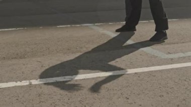 Tanınamaz haldeki enerjik erkek sporcunun düşük kesimi, güneşli kaldırımda gölgesi ile dışarıda eğiliyor.