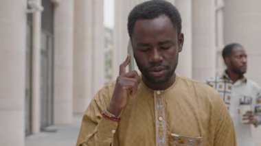 Gündüz vakti şehir merkezinde yürürken akıllı telefondan konuşan genç Afrikalı Amerikalı adamın belini kaldırın.