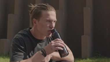 Şehirde sabah sporundan sonra su içen atletik beyaz bir adam.