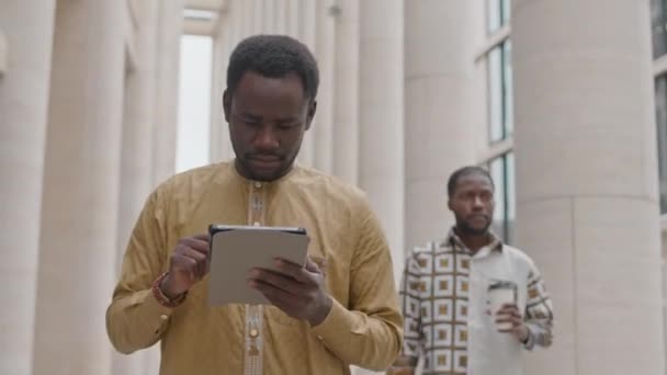 在市中心的街道上散步时 用数码平板电脑拍摄的专注的非洲裔美国年轻人的中景照片 — 图库视频影像