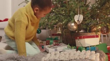 Şirin Afrikalı Amerikalı küçük kız Noel ağacının altında Noel hediyeleri arıyor.