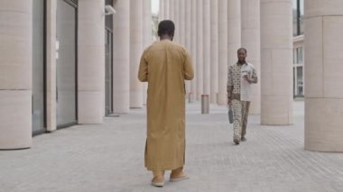 Şehir merkezindeki caddede şık kıyafetler içinde yürüyen iki yakışıklı siyahi adamın yavaş çekimleri.